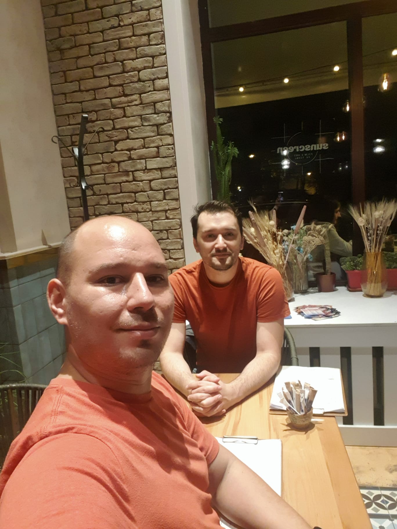 Adi and Bala wearing matching orange shirts at a café